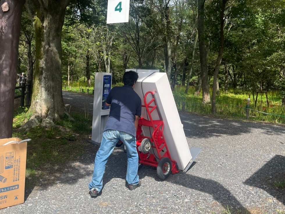 券売機をベンダートラックに乗せて砂利道を進むアトラスの代表