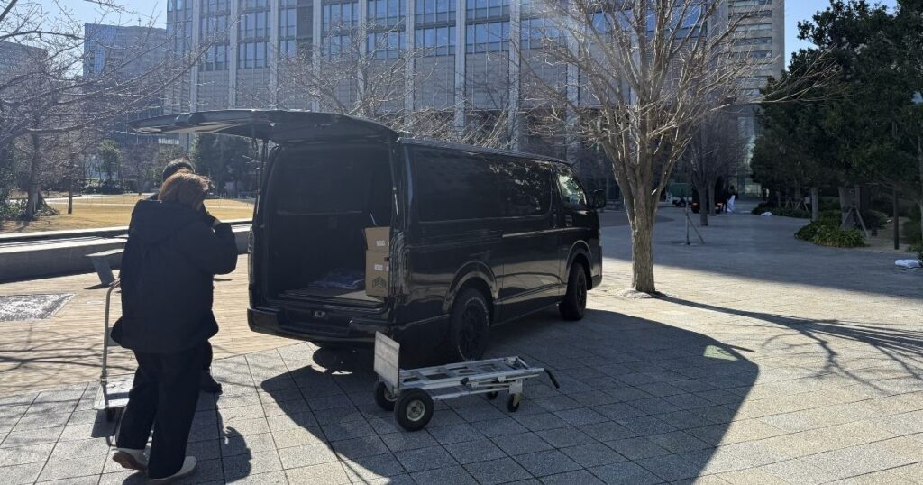 テントのペグが打てないイベント会場で荷物をハイエースから下ろすアトラスのスタッフ