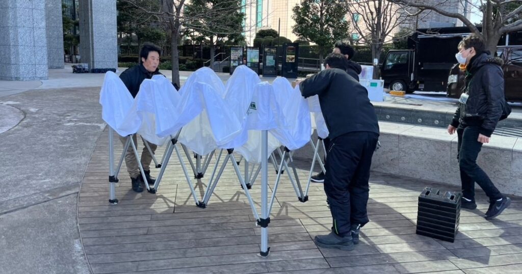 ワンタッチテントの設営方法をイベント運営のスタッフ様に実演する当社の社長とスタッフの亀山くん