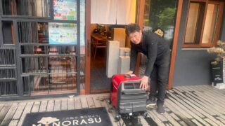 東京都大田区にあるミノラスパートナーズ株式会社の正面玄関の前で発電機を持っている亀山くん