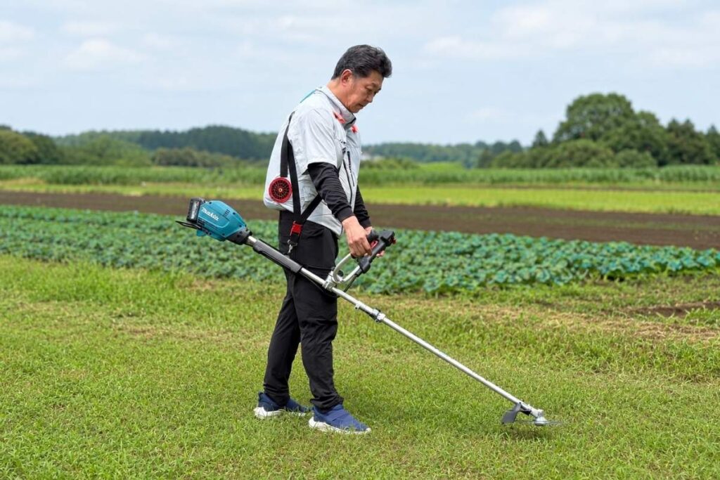 畑の雑草を草刈機で刈るアトラスのスタッフ